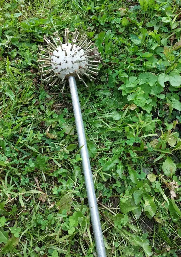 Boule en bois h&eacute;riss&eacute;e de vis, pos&eacute;e sur un lit de gravier