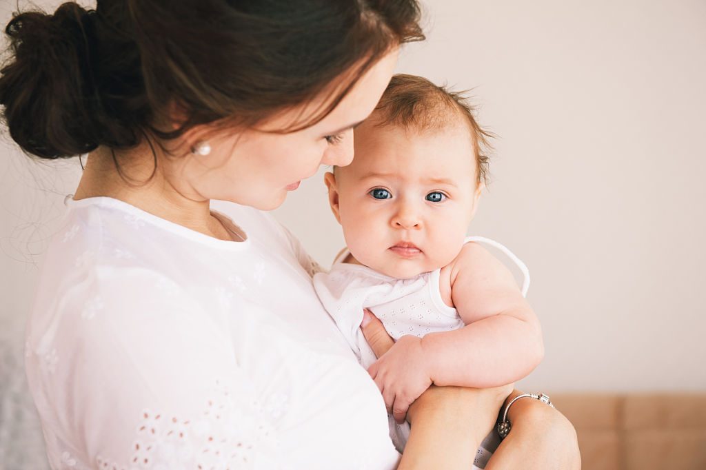 P&egrave;re soutenant la m&egrave;re qui tient enfin son b&eacute;b&eacute; dans ses bras, regard complice.