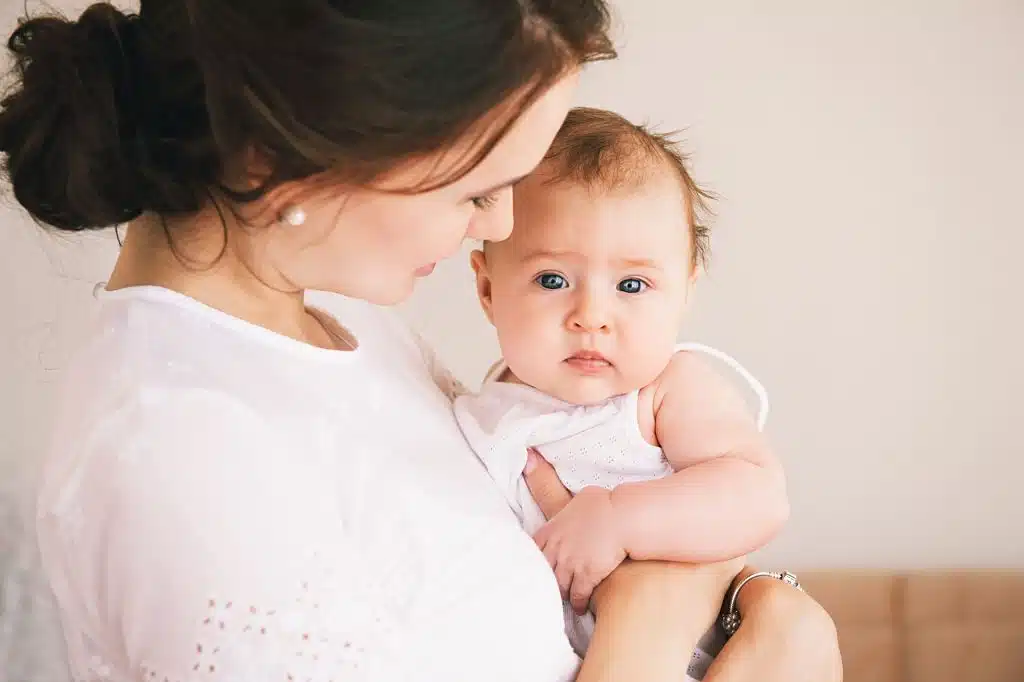 Père soutenant la mère qui tient enfin son bébé dans ses bras, regard complice.