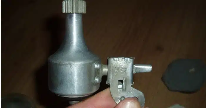 Photo en gros plan d'un objet métallique cylindrique rouillé, partiellement couvert de terre, tenu dans une main.