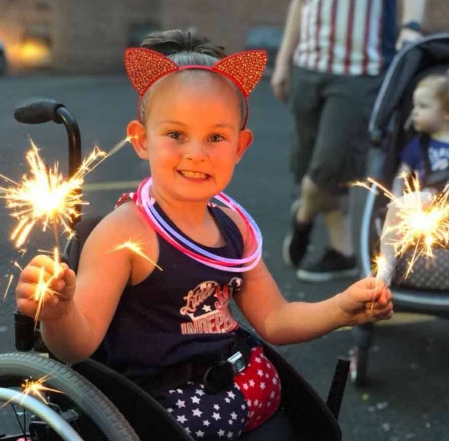 Paige souriante sur une chaise roulante tenant des bougies allumées