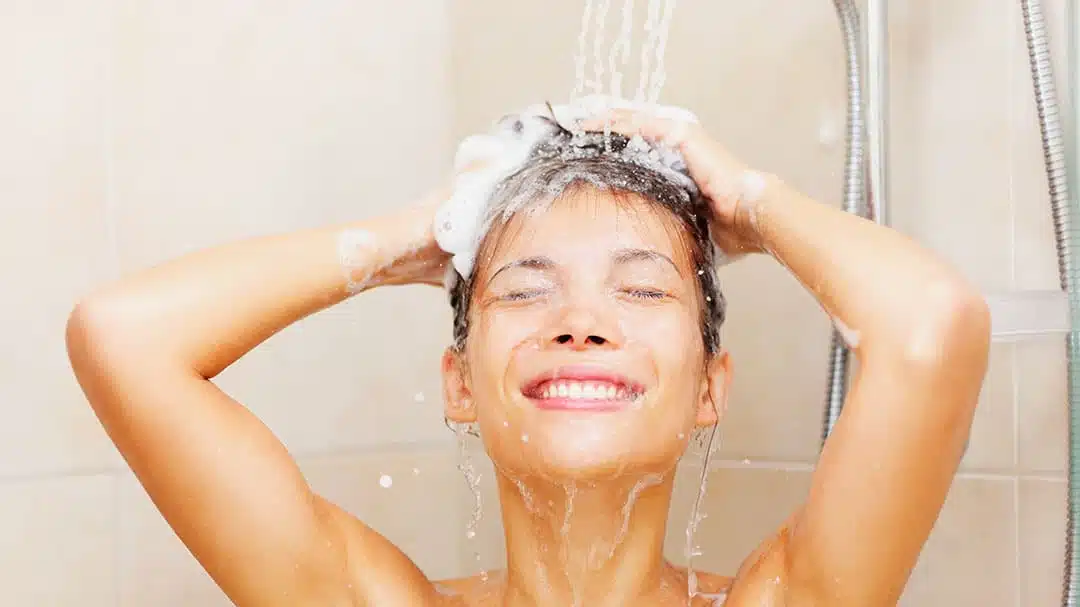 Femme souriante sous la douche en train de se laver les cheveux
