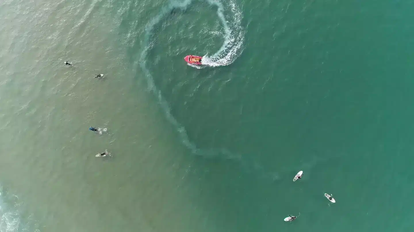 Photographie aérienne d'une scène de mer avec un bateau et des surfeurs
