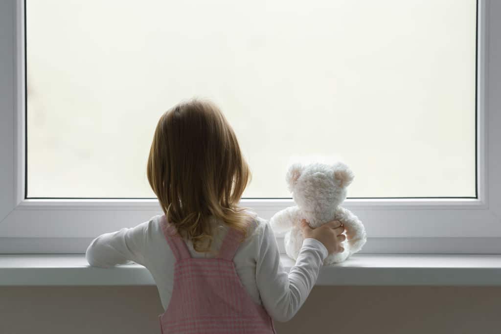 Fillette serrant un ours en peluche, regardant par la fenêtre