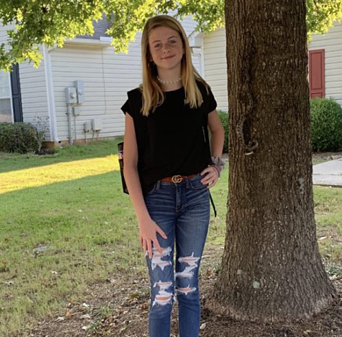 Coll&eacute;gienne souriante devant sa maison, un serpent est camoufl&eacute; sur l'arbre derri&egrave;re elle